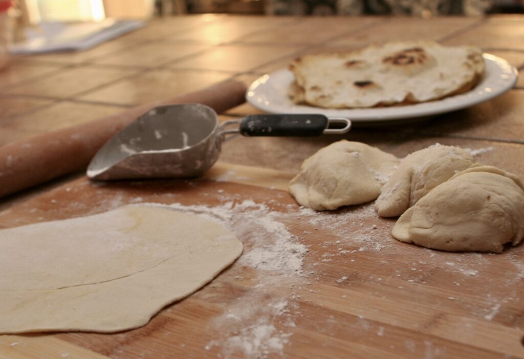 prepared and uncooked flat bread dough on floured surface