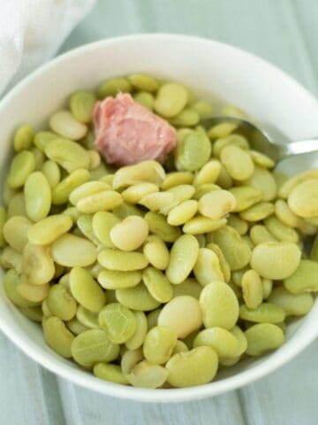 butter beans with a ham hock piece in a white bowl.