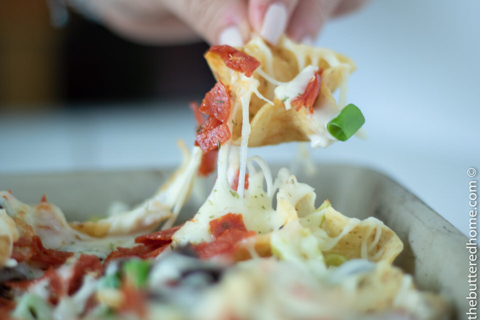 Close up photo of a loaded nacho chip being taken out of the pan to eat.