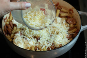 adding cheese on top of sausage and pasta before baking in oven
