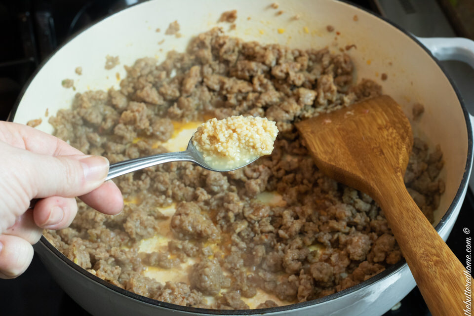 adding minced garlic to browned Italian sausage