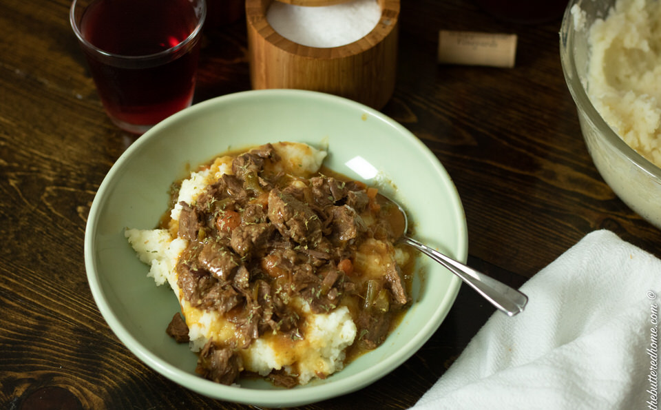 smothered beef tips in a green bowl on a dark wood table with a spoon and napkin