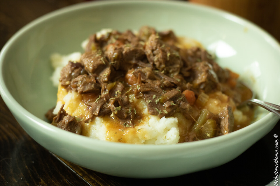 close up of smoother beef tips on bed of mashed potatoes in a green bowl
