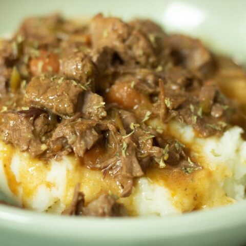 close up of smoother beef tips on bed of mashed potatoes in a green bowl