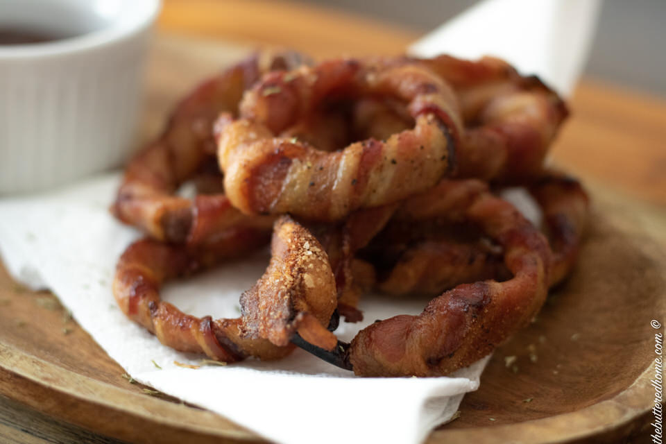 a stack of bacon wrapped onion rings on a white napkin sprinkled with parsley