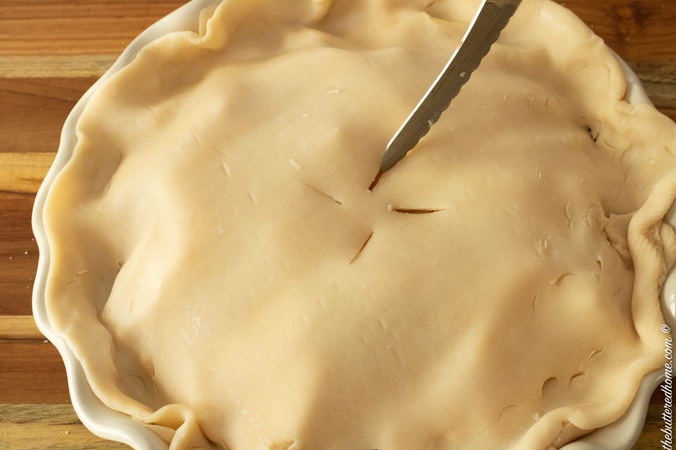 top crust on pie with a knife cutting vent holes