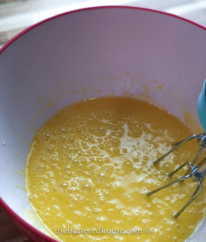 mixing eggs and sugar and syrup in a red bowl