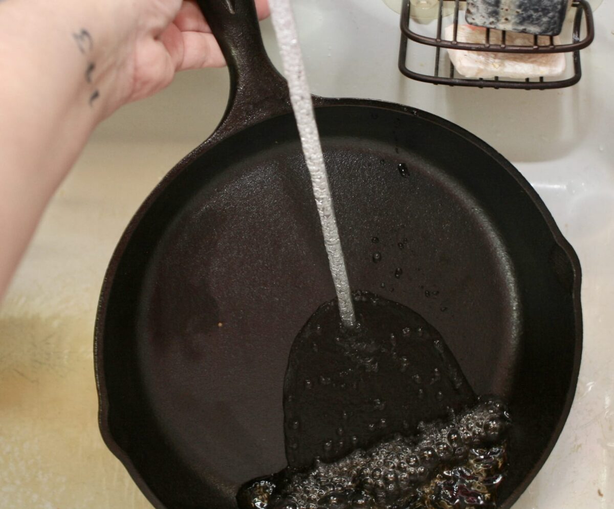 Running water into a cast iron pan under a faucet.