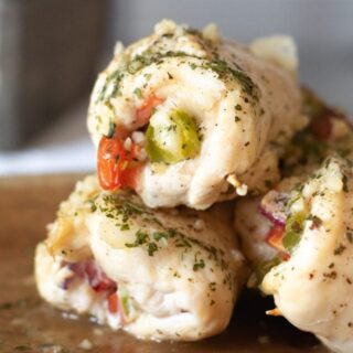 Close-up of several Super Saturday Stuffed Chicken Roll Ups, filled with tomatoes and green peppers, topped with herbs and spices on a wooden surface. These delicious roll ups are perfectly cooked and beautifully garnished for a satisfying meal.