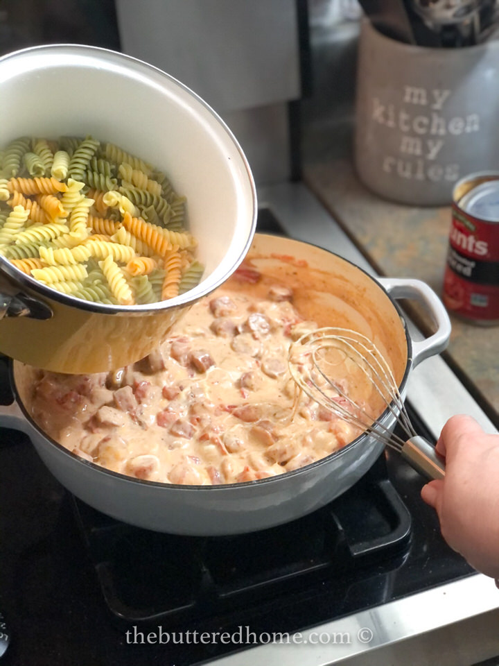 adding cooked pasta to sausage and cream sauce