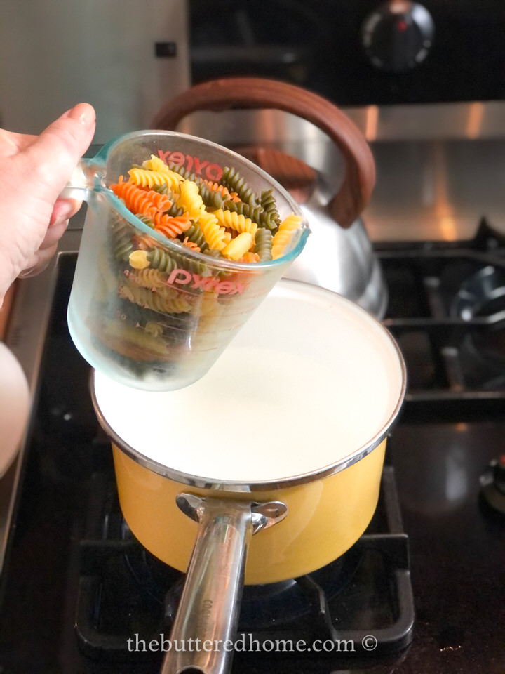 pouring dry rotini pasta into boiling water