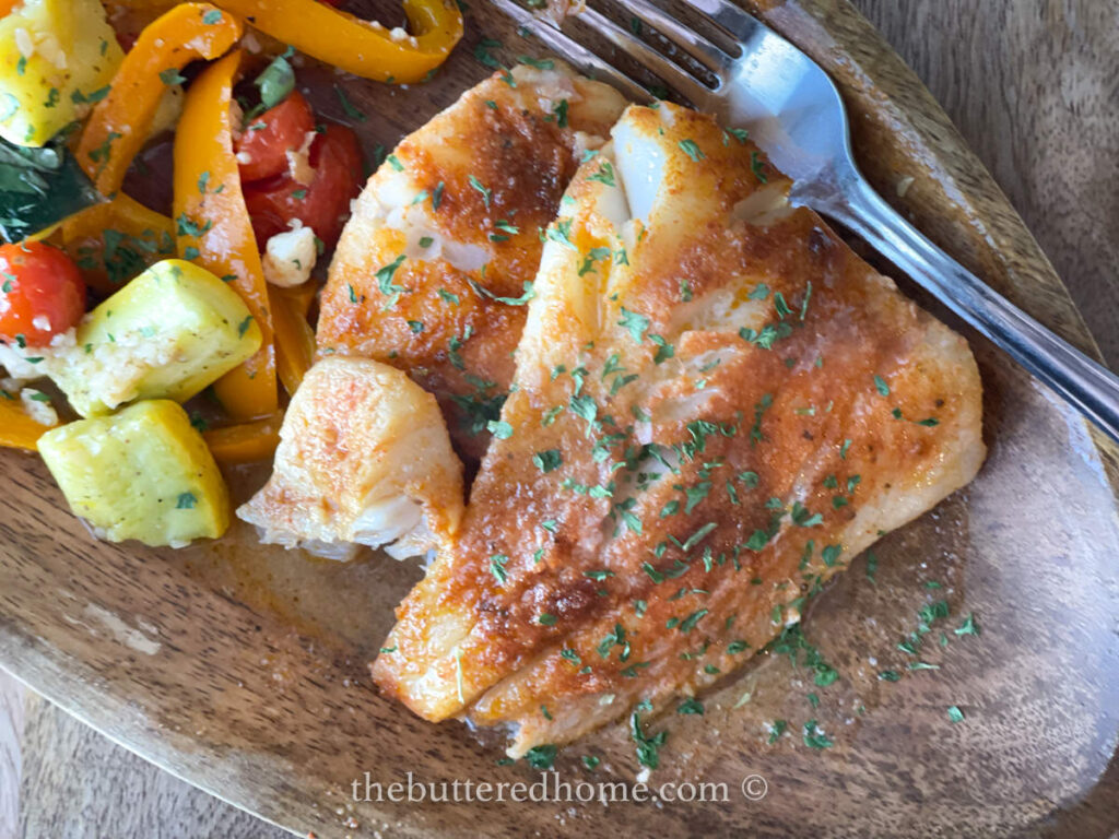 cooked cod with colorful veggies on a wooden plate