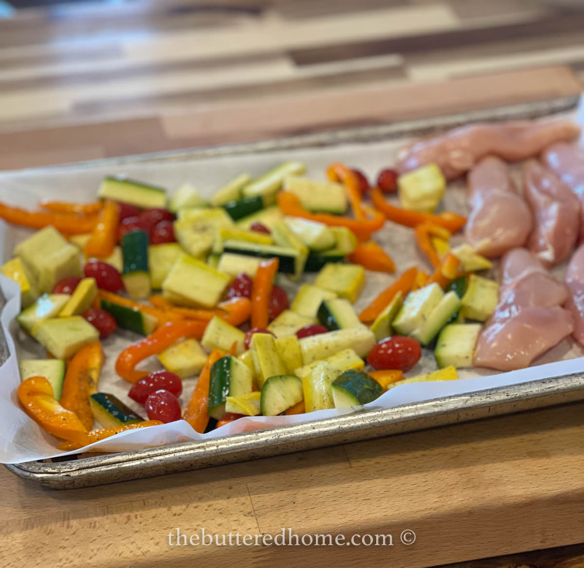 vegetables and uncooked chicken on sheet pan lined with parchment