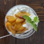 peaches with a green mint leaf sitting on a dish of cream