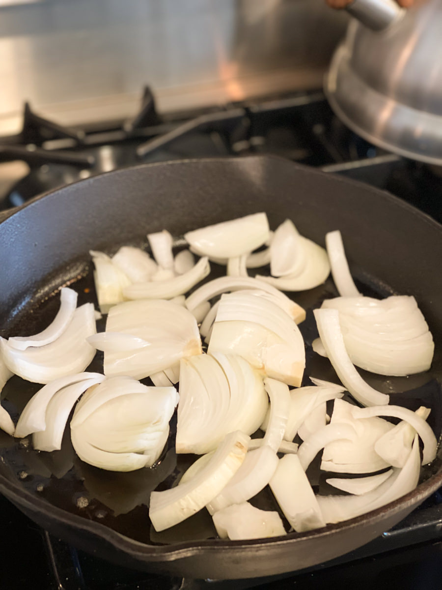 sliced white onions in a cast iron skillet