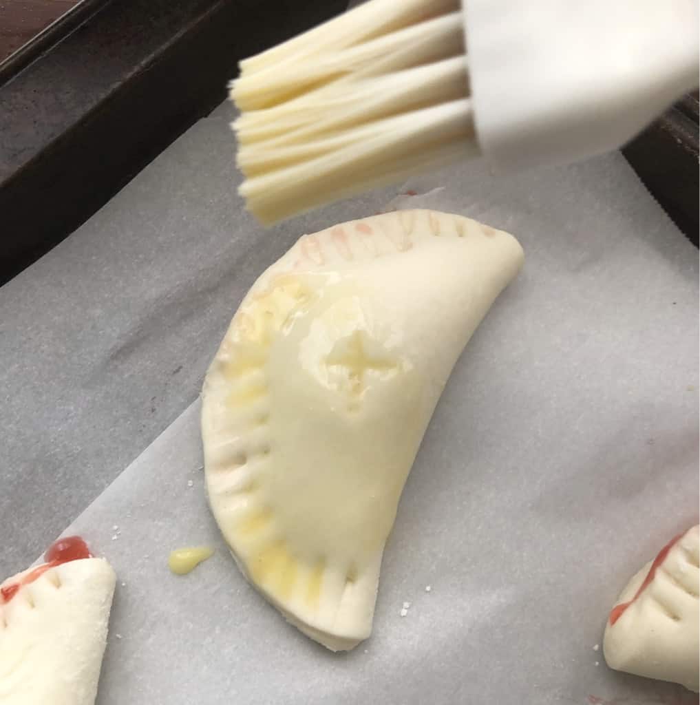 Brushing hand pies with pastry brush and egg wash.
