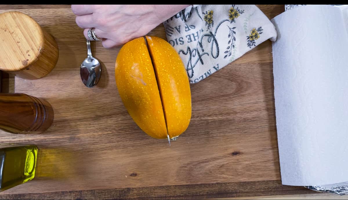 Carefully cutting spaghetti squash on a wooden board into two halves.