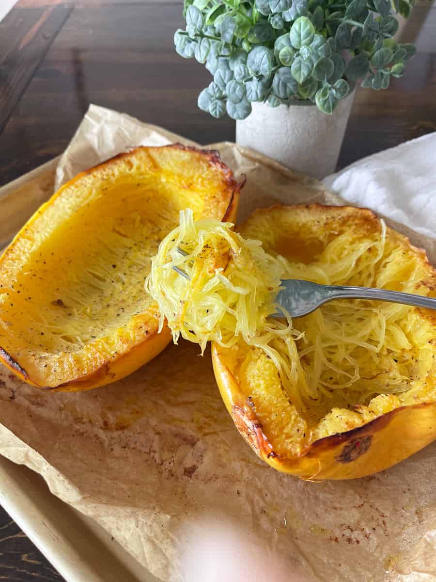 Sheet pan of spaghetti squash with a fork and a plant in the background.