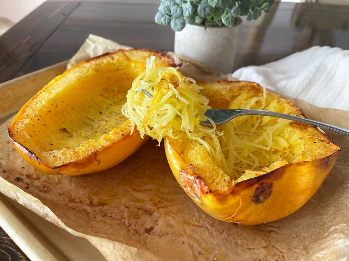 A cooked yellow spaghetti squash on a pan with a fork full nearby.