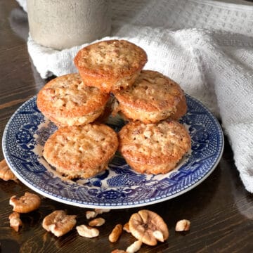 pecan pie muffins on a blue and white plate with pecan halves scattered in front.