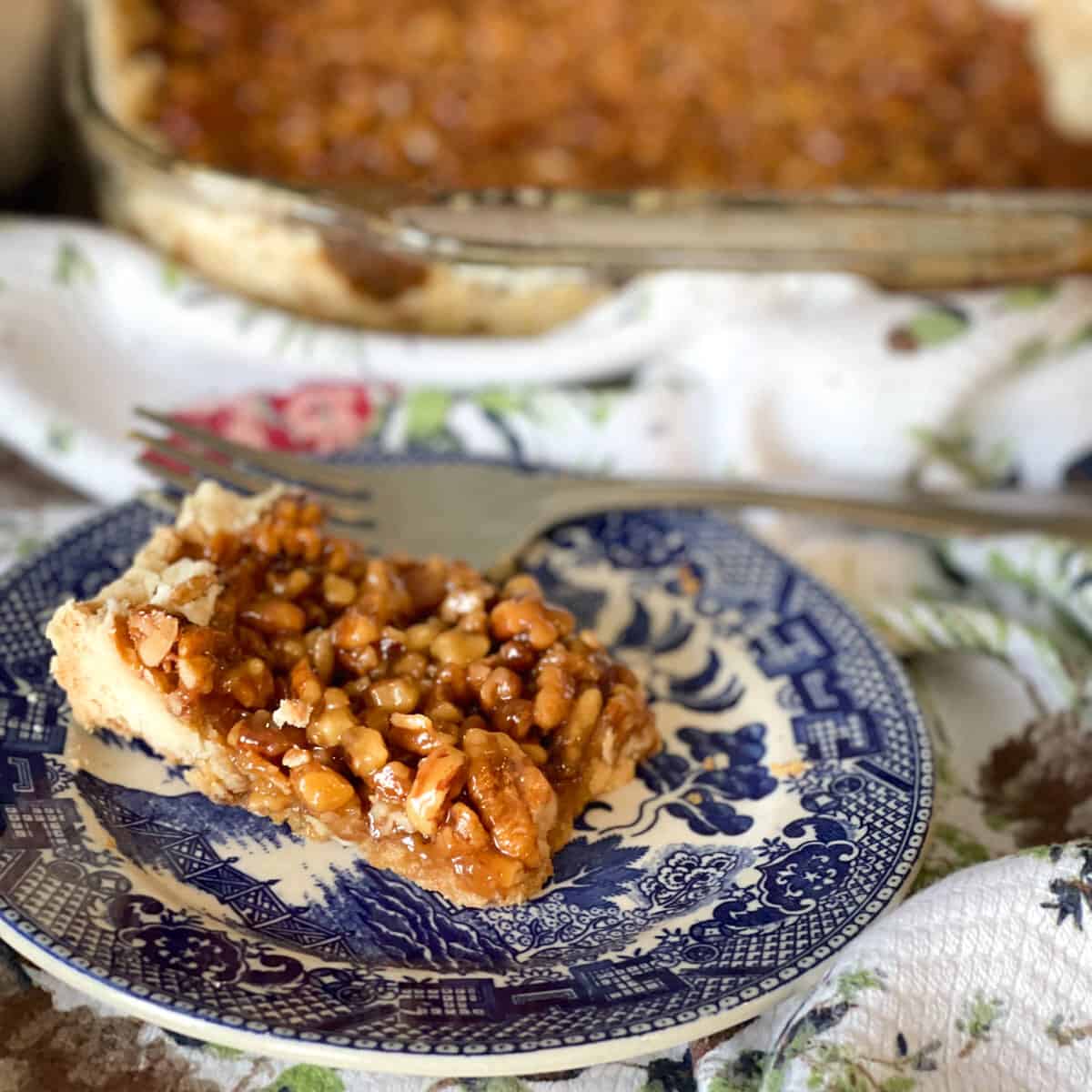 one pecan square slice with large dish in background.