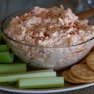 pimento cheese in a clear bowl with crackers and celery on a plate.