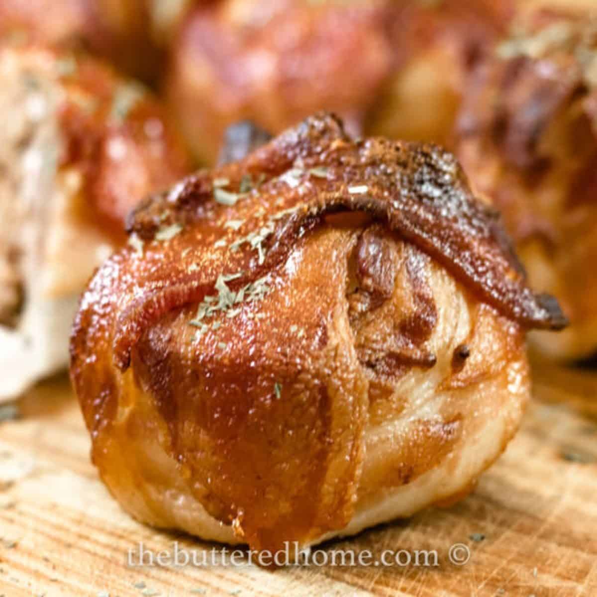 a bacon wrapped onion meatball bomb on a wooden board