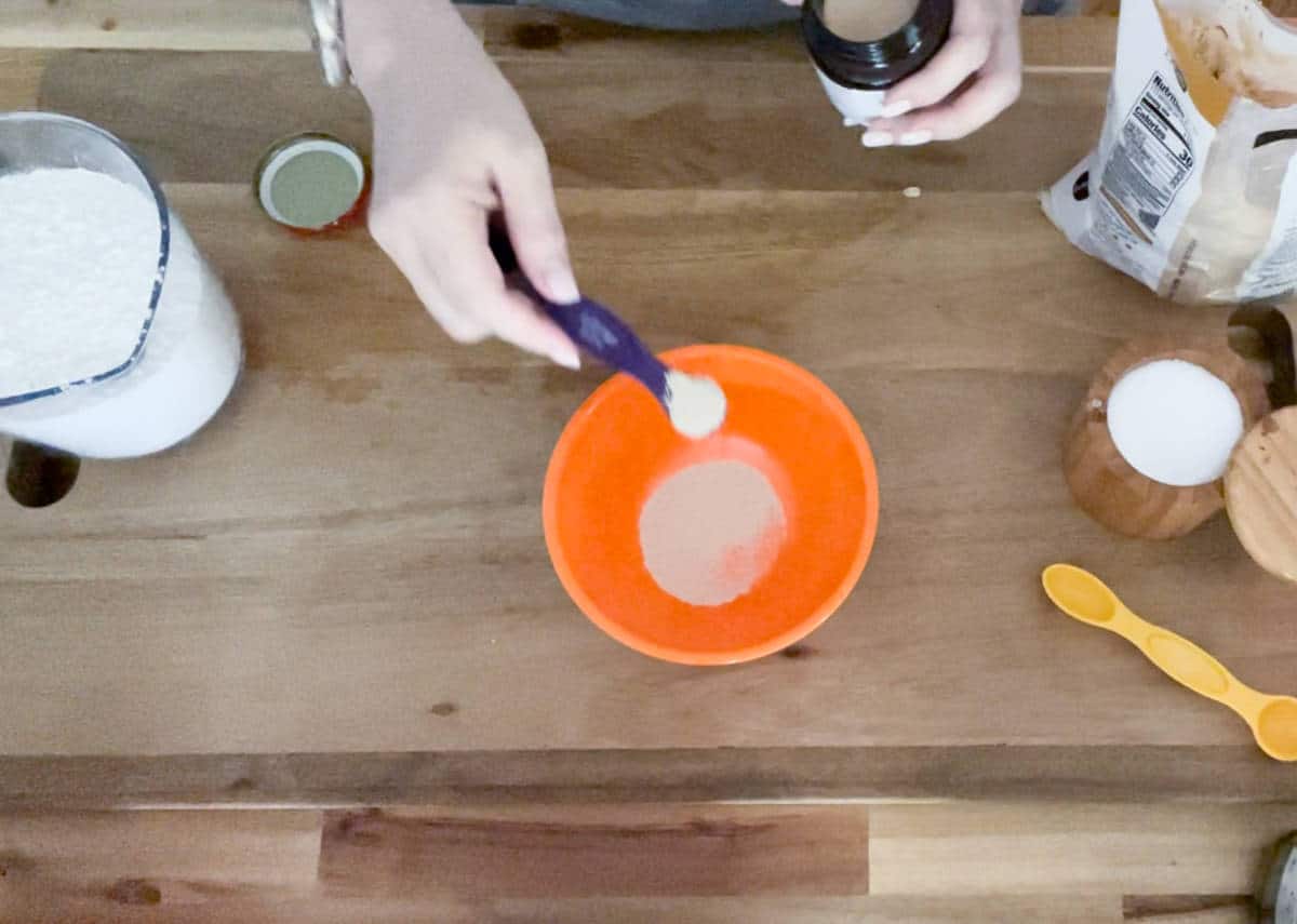Adding quick rise yeast to an orange bowl.