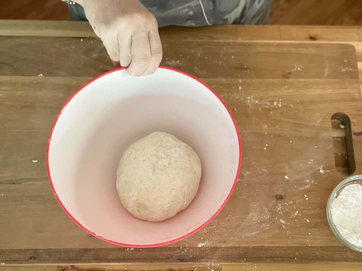 Putting dough in a greased white and red bowl.