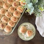 Two dinner rolls on a plate with a pan full in the background.