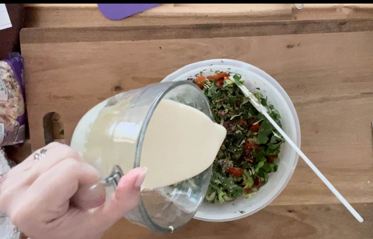 Pouring dressing over greens in a white bowl.