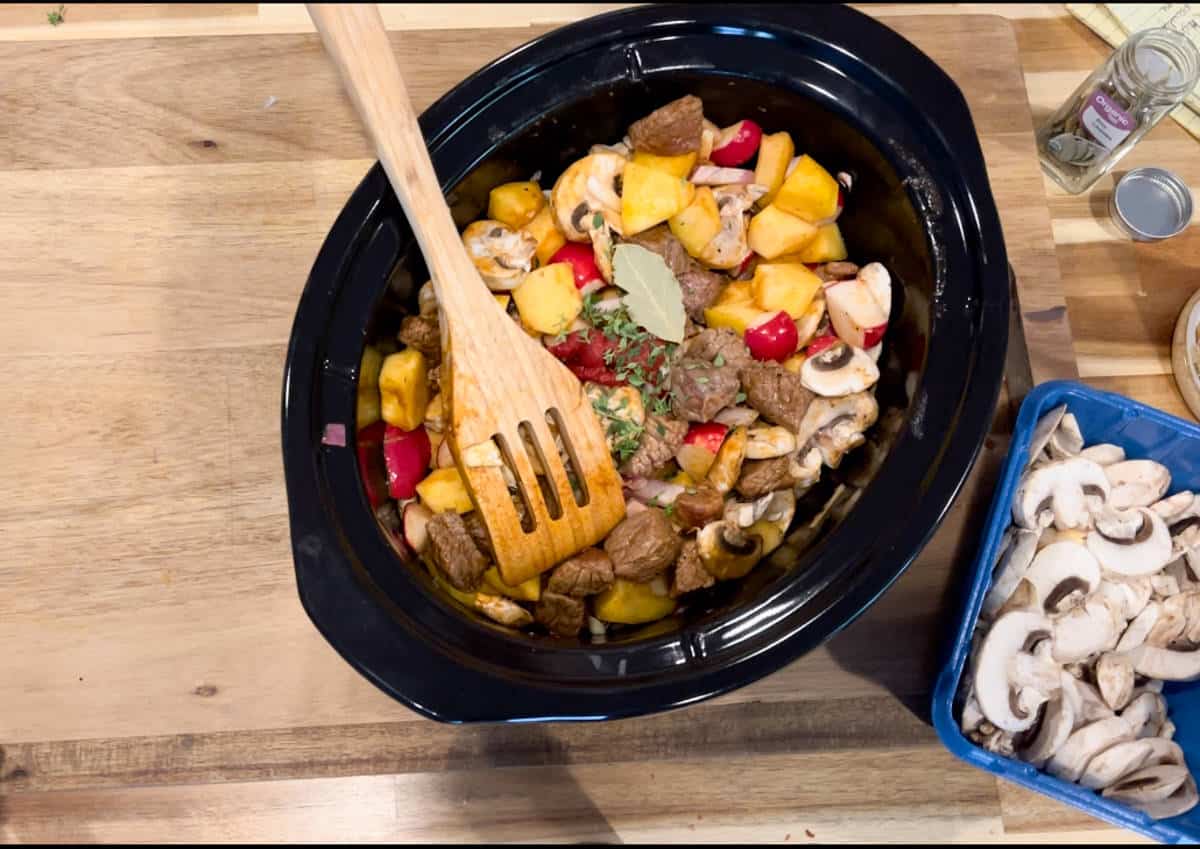 A black crock pot with beef and vegetables.