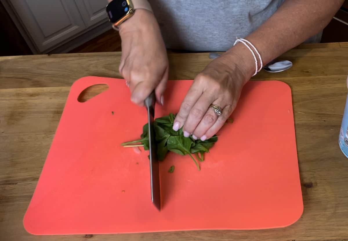 Chopping spinach on a red cutting board.