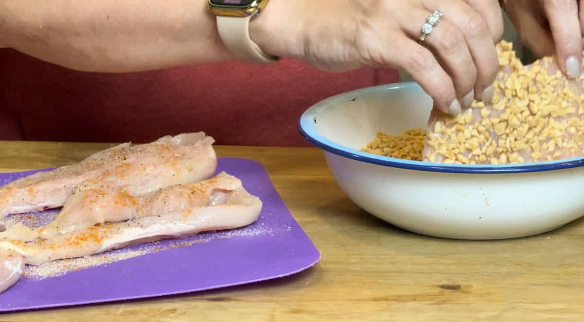 Coating the chicken breast in chopped peanuts.