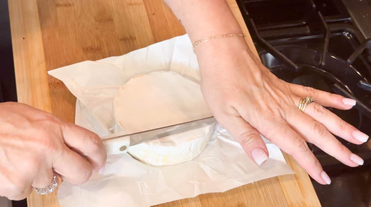 Carefully cutting horizontally across the top of the brie.