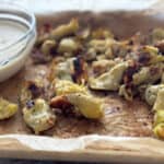 Crispy artichoke hearts on a serving pan with garlic dipping sauce.
