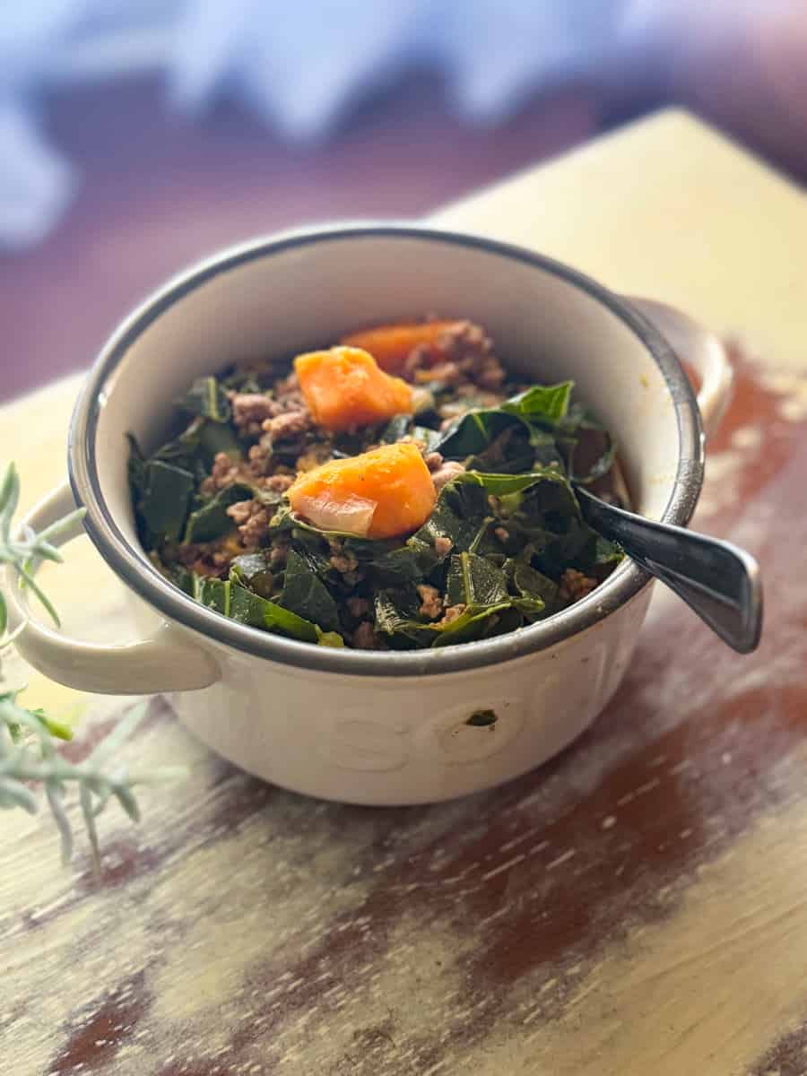 bowl of sweet potato and collard green soup on a white table.