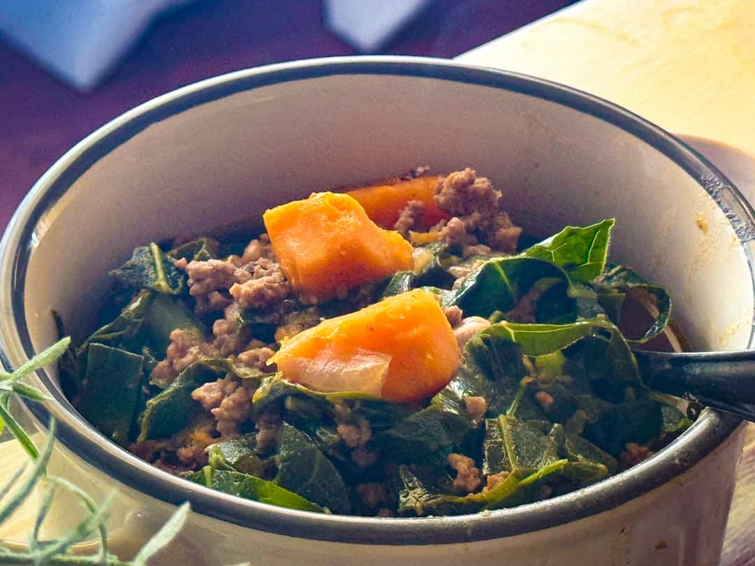 Close up of sweet potatoes and collard greens in soup.