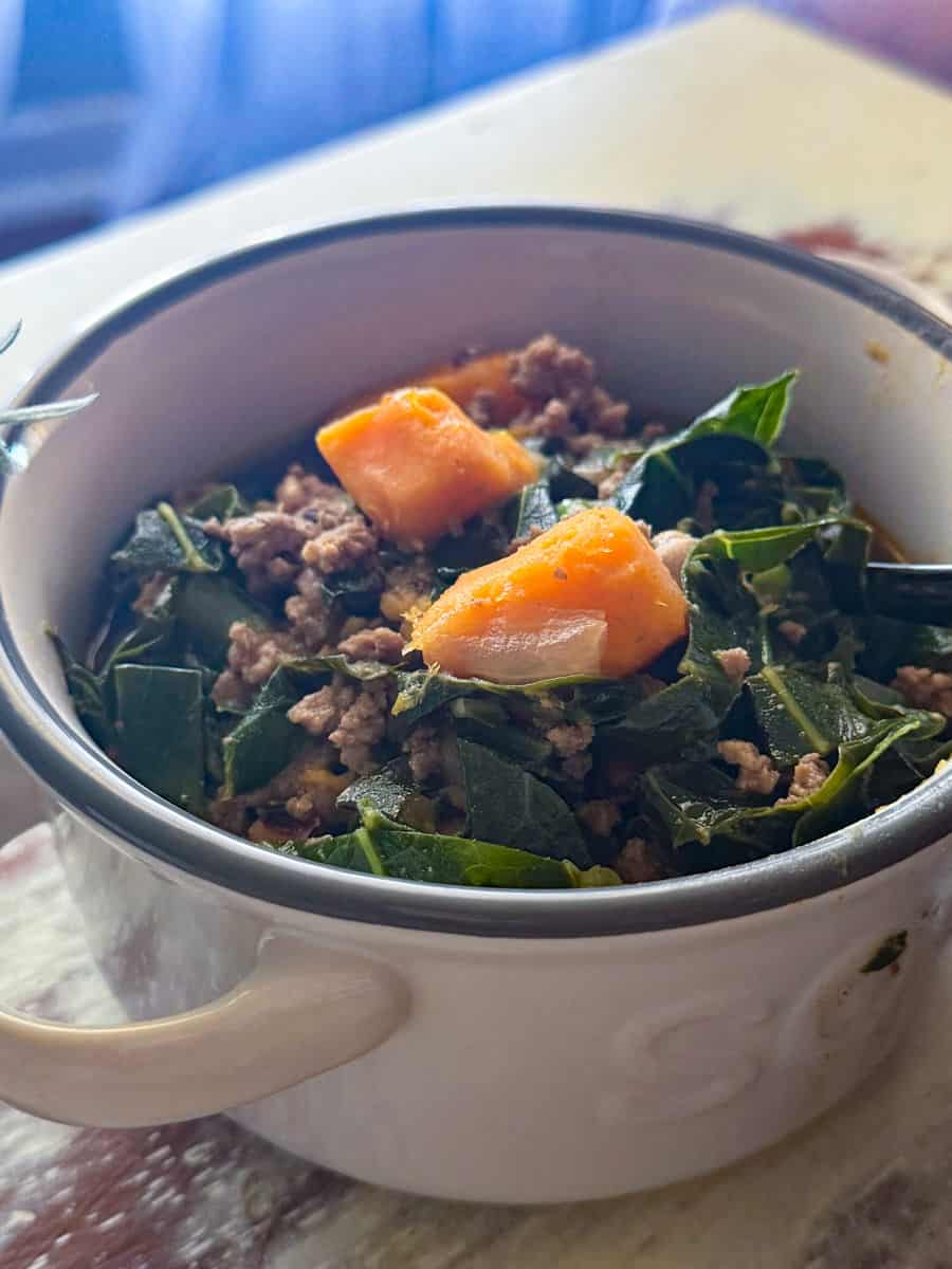 A white soup bowl of sweet potato and collard soup.