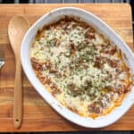 Sour cream beef bake in a white casserole dish on wooden surface with a wooden spoon.