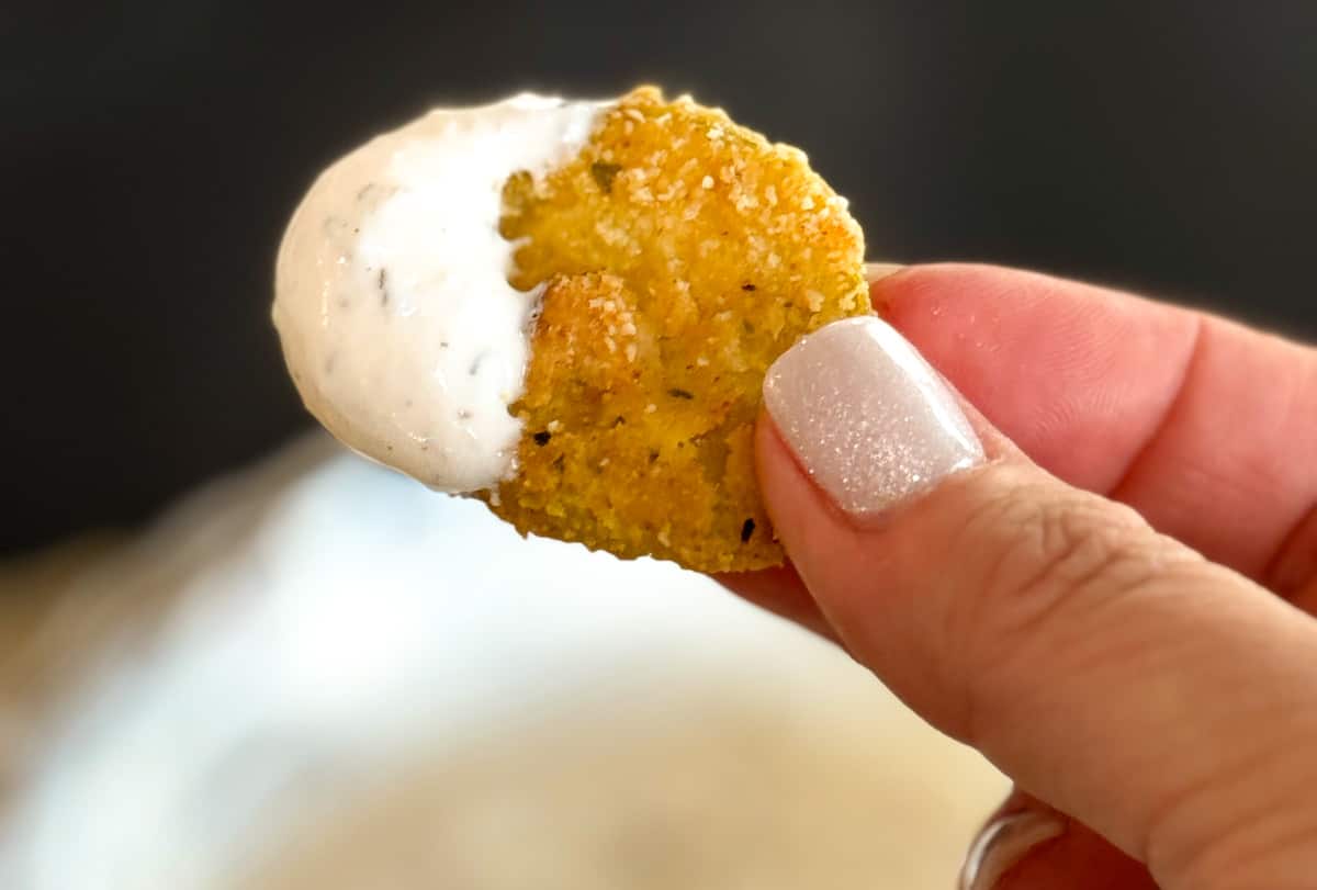 A hand holding an oven fried pickle dipped in ranch dressing.