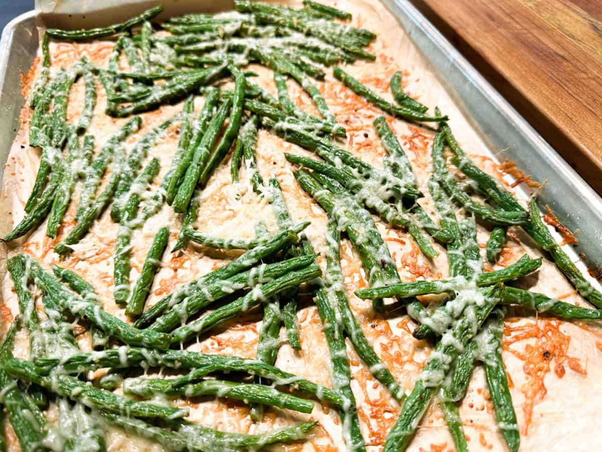 A tray of roasted green beans with melted cheese on a baking sheet.