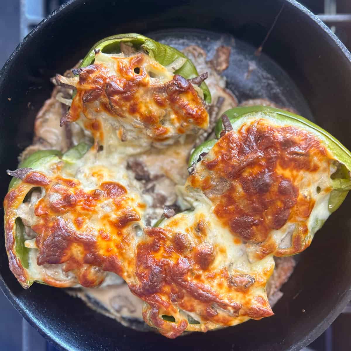 Stuffed bell peppers with melted cheese on top, cooked in a black pan.