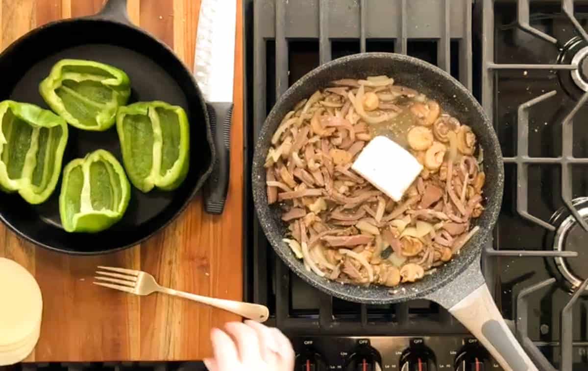 Cooking ingredients on a stovetop, with sliced green bell peppers in a skillet on the left and a mix of mushrooms and meat in a skillet on the right with a spatula.