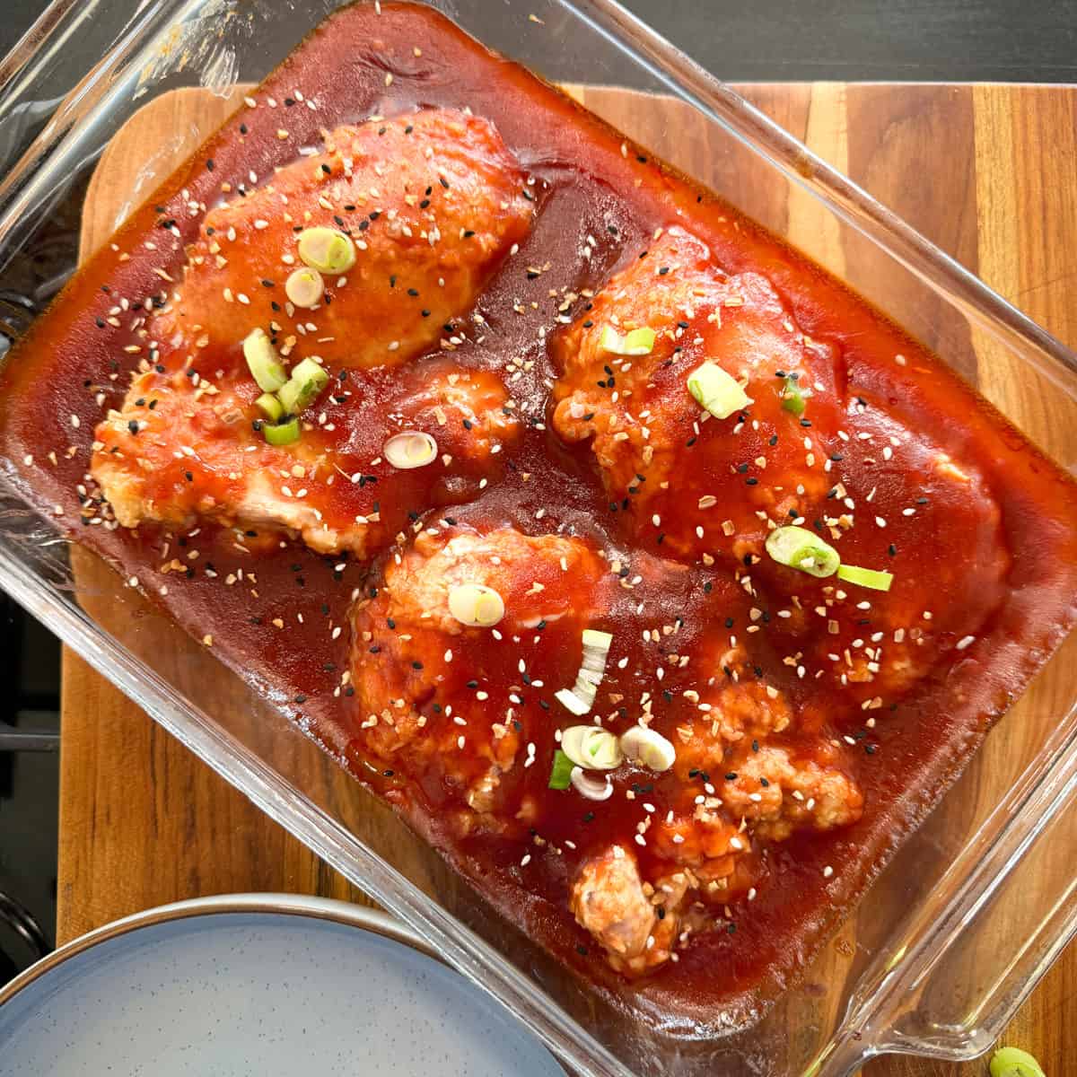 Sticky chicken in honey sauce garnished with sesame seeds and chopped green onions in a glass dish.