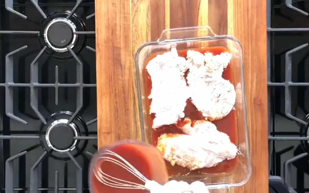 Sticky honey sauce being poured onto breaded chicken in a glass baking dish.