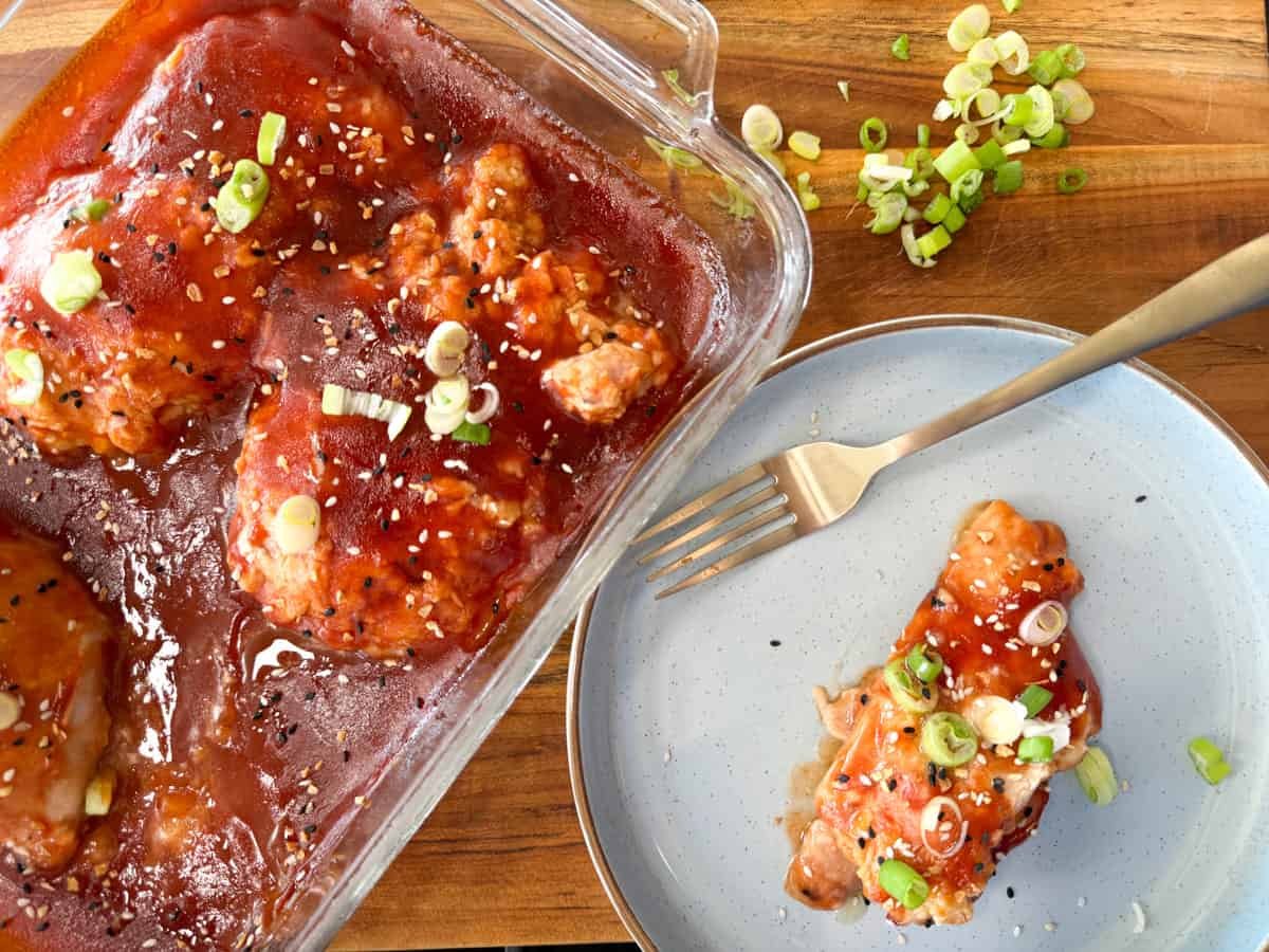 Marinated chicken in a glass dish alongside a single served portion on a blue plate, garnished with green onions.