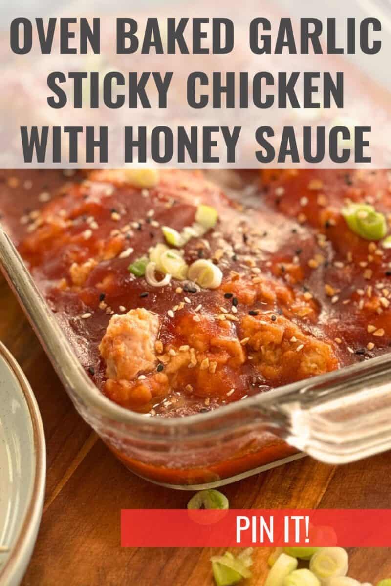 A glass baking dish containing oven-baked garlic sticky chicken with honey sauce, garnished with sesame seeds and chopped green onions, ready to serve.