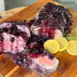 Pan seared filet enhanced with a blueberry glaze, elegantly sliced on a wooden board. Garnished with fresh rosemary and lemon slices for a delightful finish.
