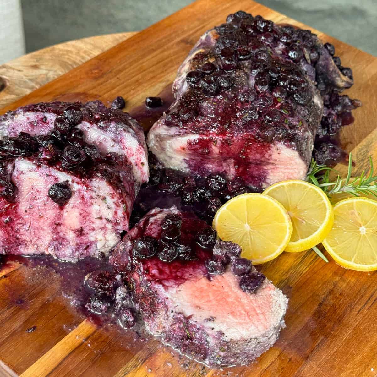 Pan seared filet enhanced with a blueberry glaze, elegantly sliced on a wooden board. Garnished with fresh rosemary and lemon slices for a delightful finish.